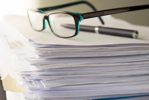 stack of paperwork with a pair of black glasses and pen sitting on top